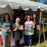 four authors holding their books, under a tent on a sunny day