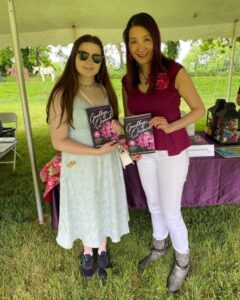 Woman with sunglasses and sundress standing beside author Carol VanDenHende. Both are holding copies of Goodbye, Orchid