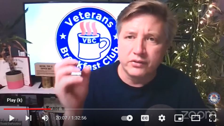 Blond haired man in black t-shirt with Veterans Breakfast Club logo behind him